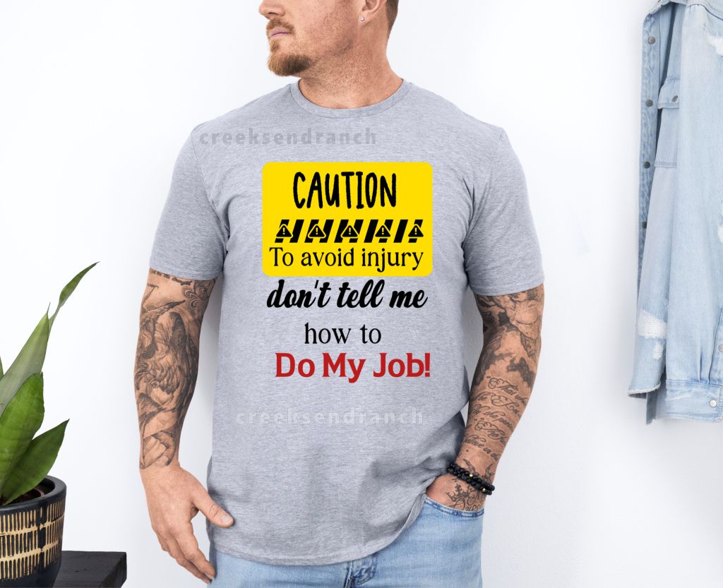 Man wearing a gray T-shirt with a bold yellow caution graphic that reads, 'To avoid injury, don’t tell me how to do my job'.