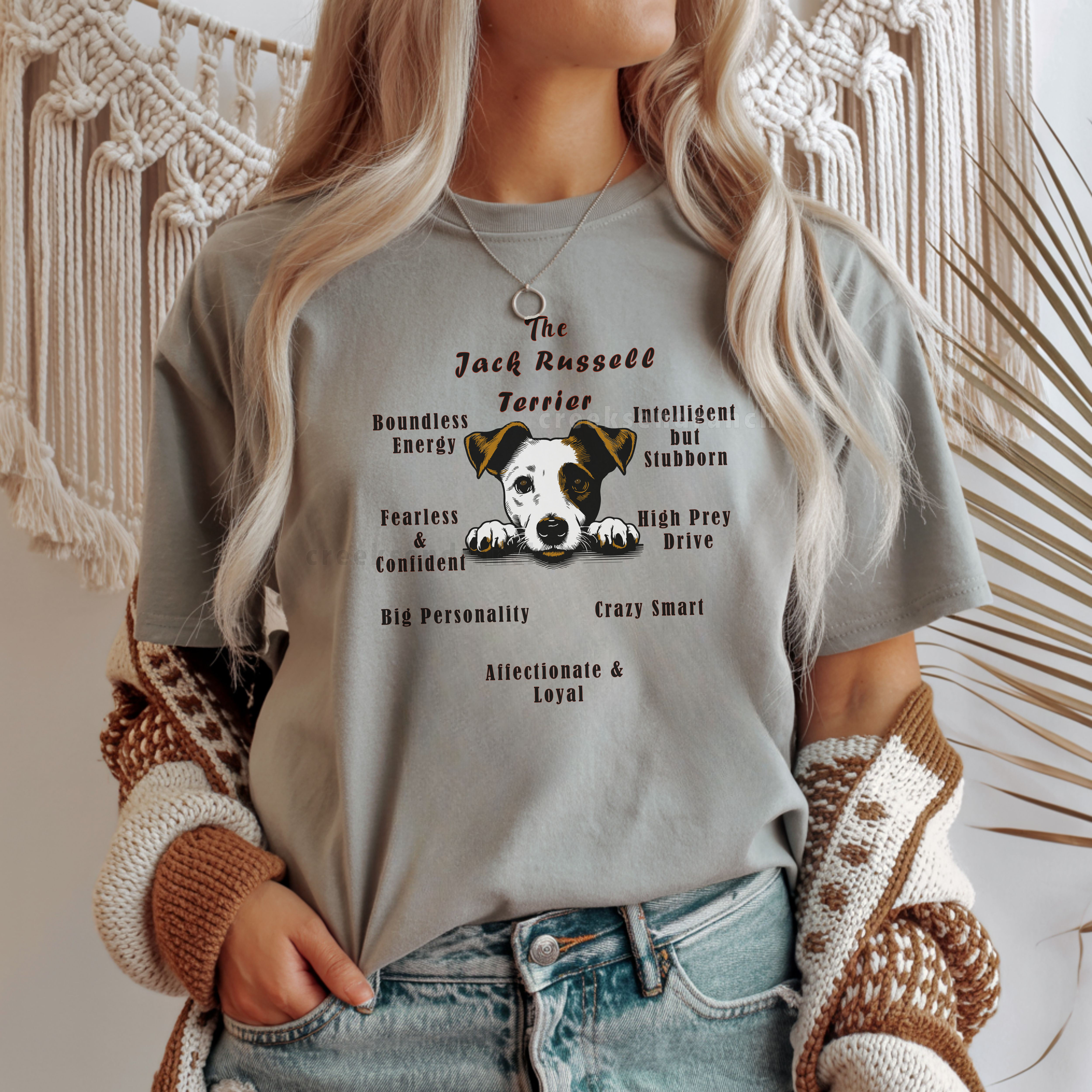 Person wearing a gray graphic T-shirt with a Jack Russell Terrier illustration and bold text, tucked into light-wash jeans, a brown-and-cream knitted cardigan draped over shoulders.