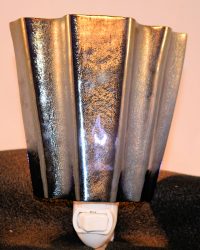 Shiny ribbed metal sculpture with gold and dark tones standing on a black surface, seen from the side.